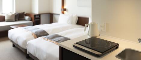 A hotel room with a bed, a coffee maker, a kettle, and a built-in induction cooktop on the counter.