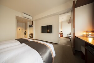 Habitación de hotel con una cama grande, un escritorio con lámpara, un televisor de pantalla plana montado en la pared y una puerta que da a otra habitación.