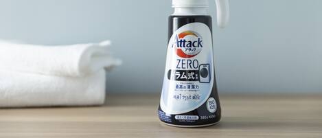Una botella de detergente para ropa Attack Zero sobre una superficie de madera, con una toalla blanca al fondo.