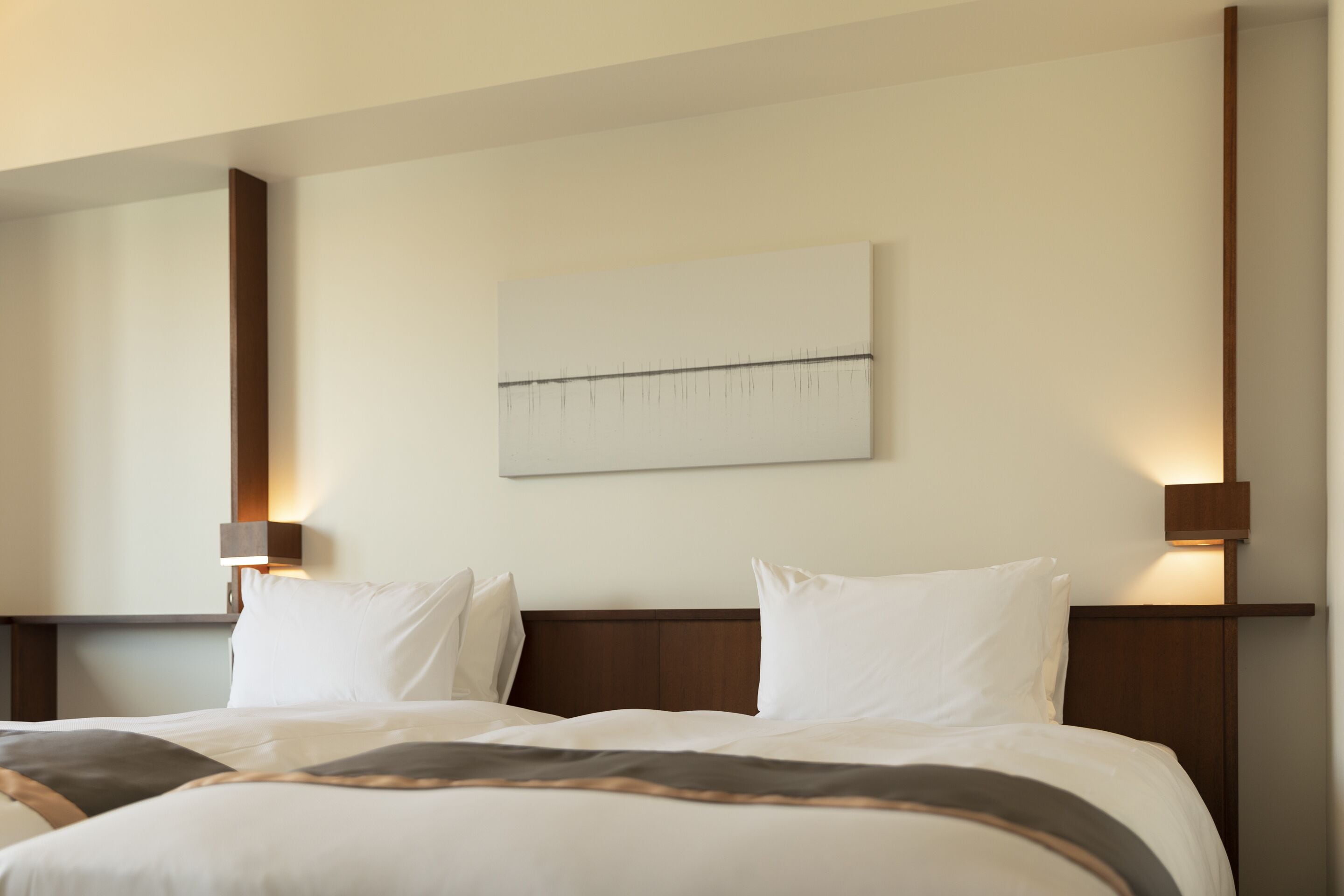 A hotel room with a large bed, two bedside lamps, a wall-mounted artwork, and a wooden headboard.