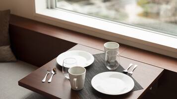 A dining table set with plates, a mug, and cutlery near a window.