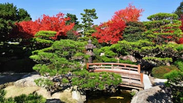 Un giardino giapponese tradizionale con un ponte di legno, una pagoda in pietra e diverse piante e arbusti.