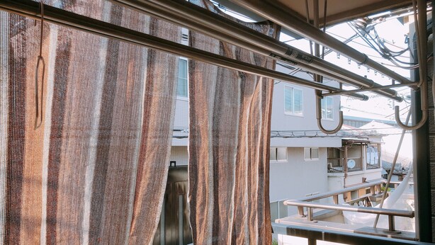 Vista a través de una ventana con cortinas a rayas, barandilla metálica y edificios visibles al exterior.