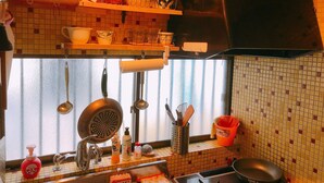 A kitchen with a tiled backsplash, hanging utensils, a stove, and a window with blinds. - Ryokoheya Tenchokan (Osaka)
