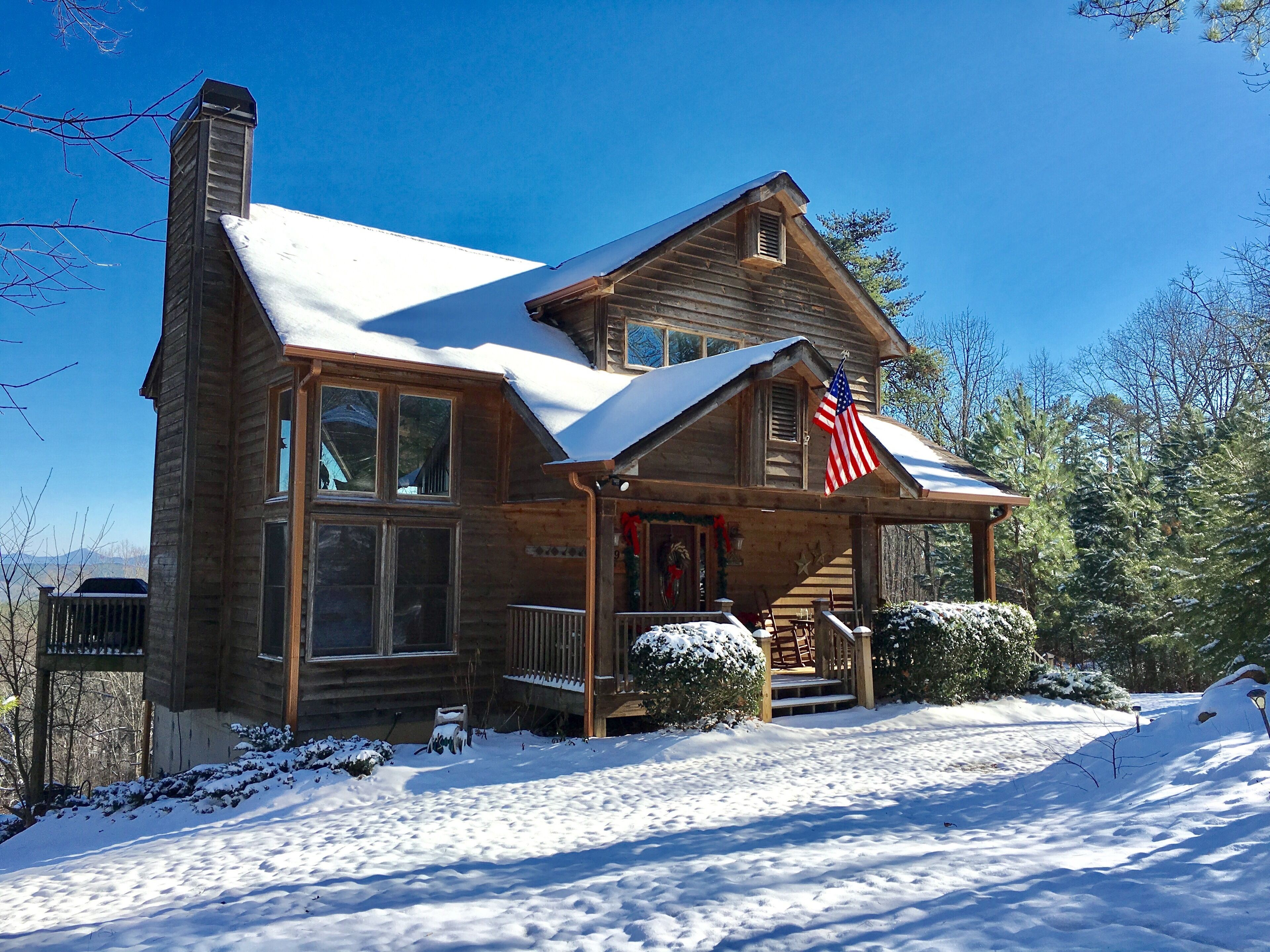 A wooden cabin with a snow-covered roof and a porch with an American flag.