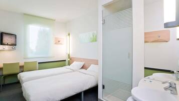 Ein Hotelzimmer mit zwei Betten, einem Fernseher, einem Fenster, einem Badezimmer mit Waschbecken und Spiegel sowie einer Tür mit Milchglasfenster.
