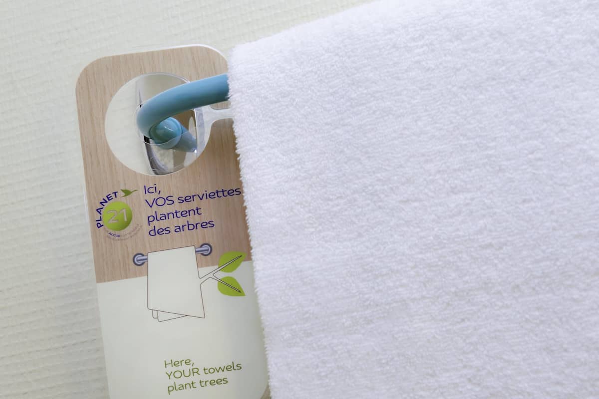 A tag attached to a towel with text in French about towel reuse for tree planting.