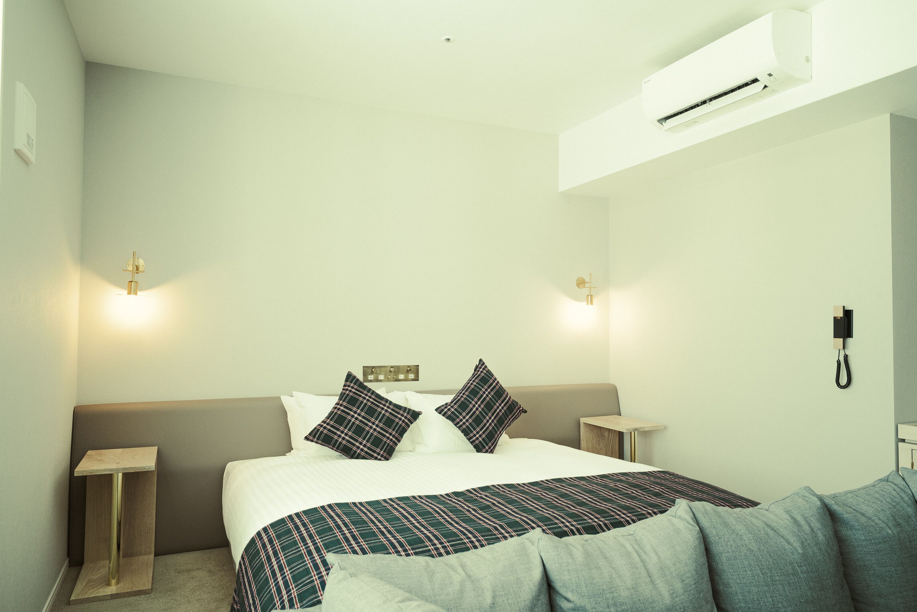 Hotellihuone, jossa on sänky, yöpöydät, seinään asennettu puhelin ja ilmastointilaite.