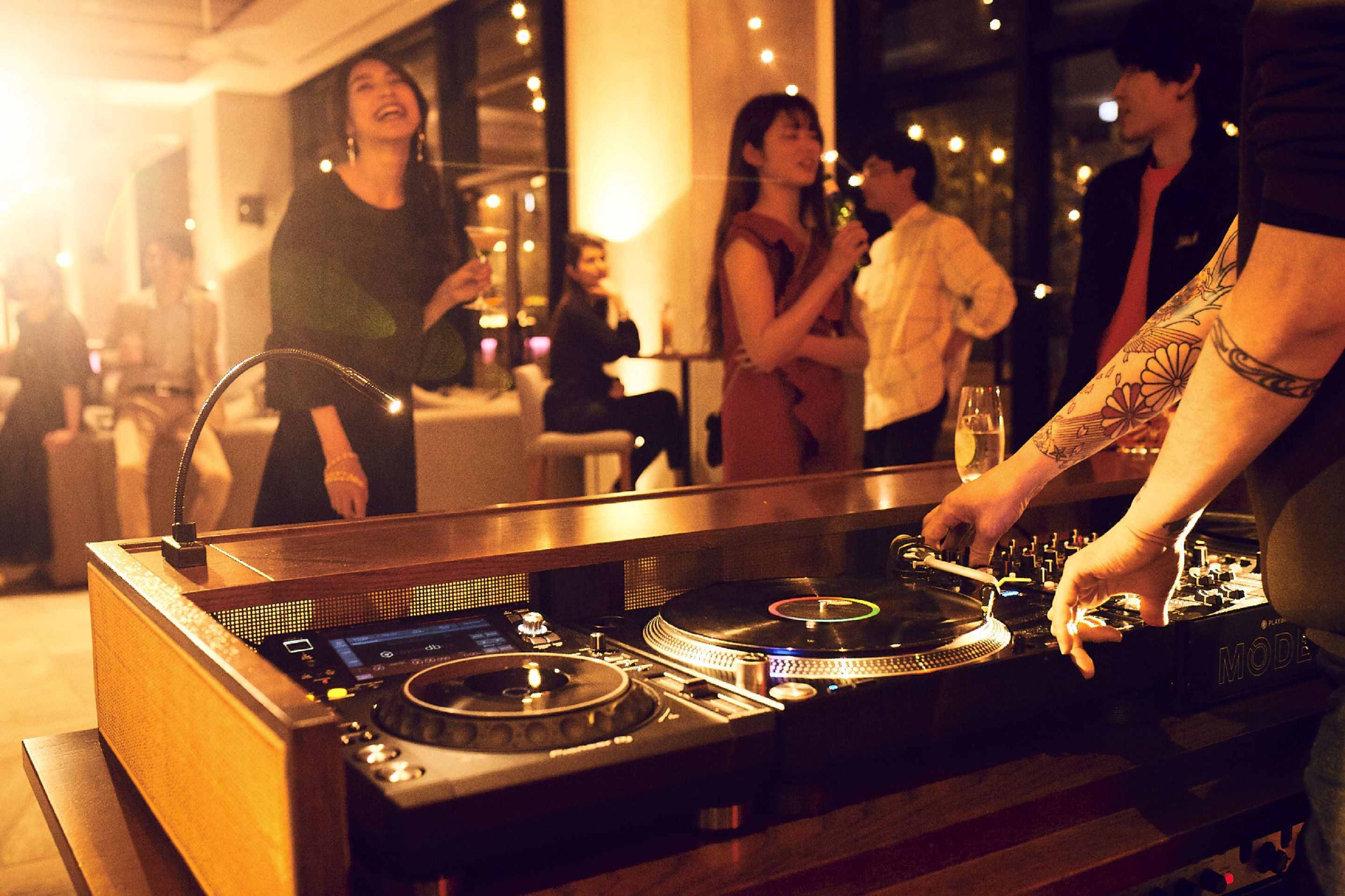 Une table de DJ avec des platines et une console de mixage, entourée de personnes dans un espace intérieur à la lumière tamisée.