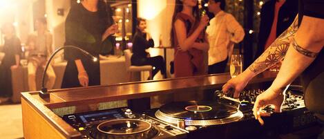 Une table de DJ avec des platines et une console de mixage, entourée de personnes dans un espace intérieur à la lumière tamisée.
