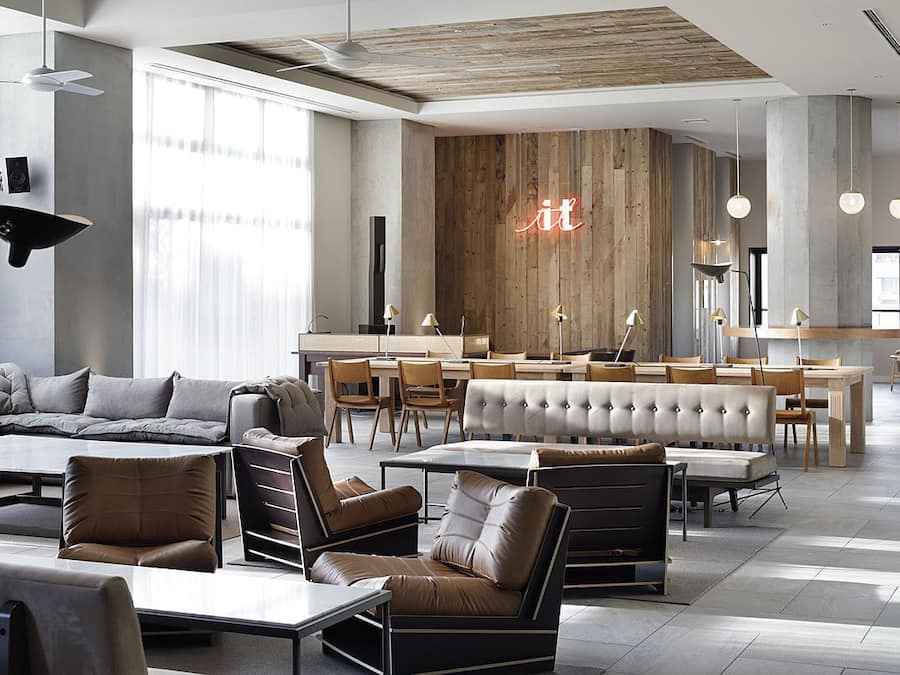 A modern hotel lobby with a central seating area, a wooden accent wall, and a neon sign.