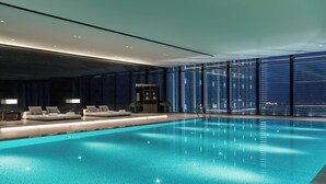 An indoor swimming pool with a modern design, featuring a clear blue pool, a seating area with cushions, and a view of the cityscape through large windows. - Niccolo Changsha (Changsha)