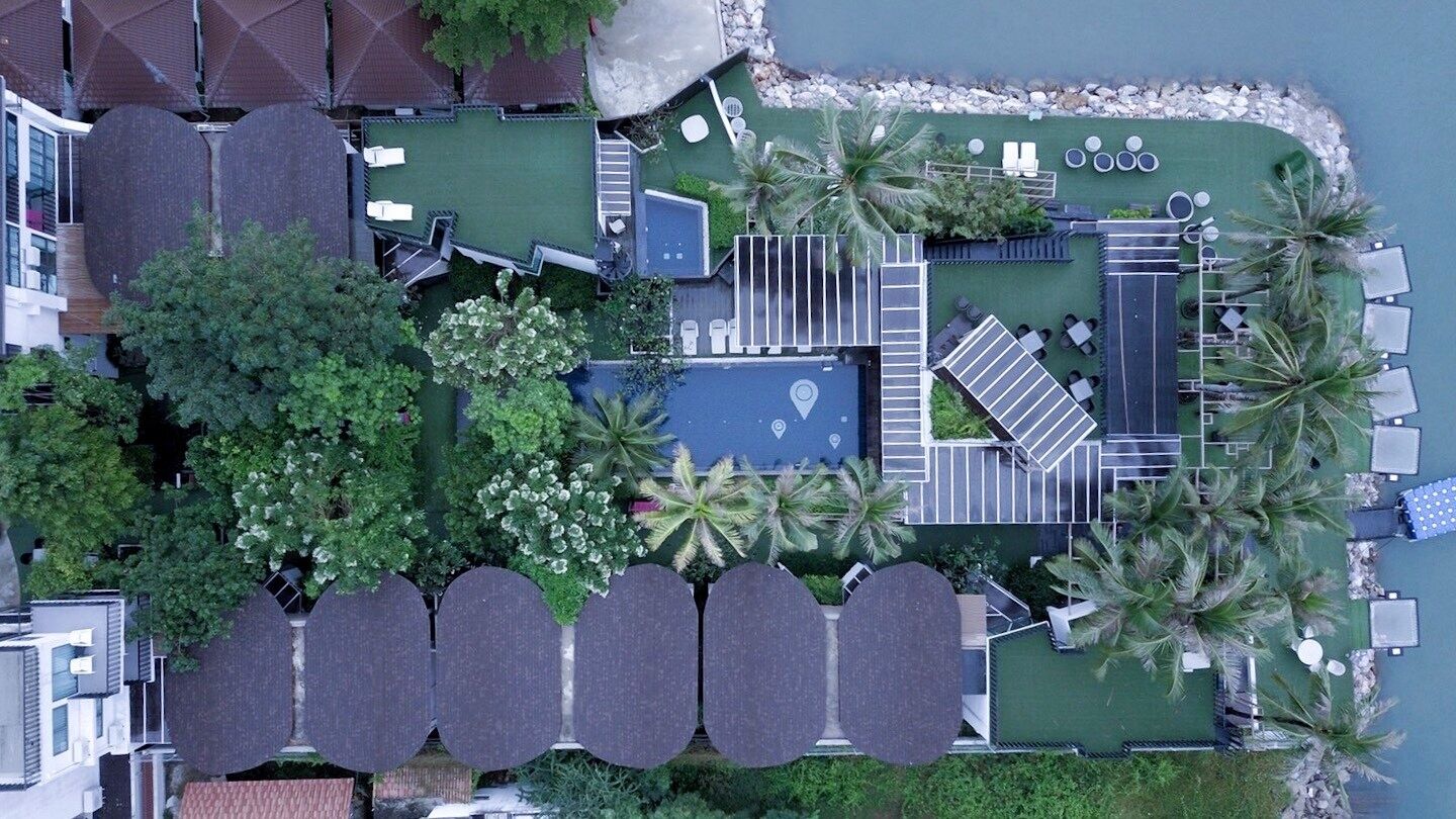An aerial view of a resort with a pool, sun loungers, palm trees, and a small building.