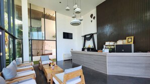 A modern reception area with a wooden reception desk, a flat-screen TV, and a dark wooden wall. - Eco Moment Beach Resort Hadchaosamran (Ban Laem)