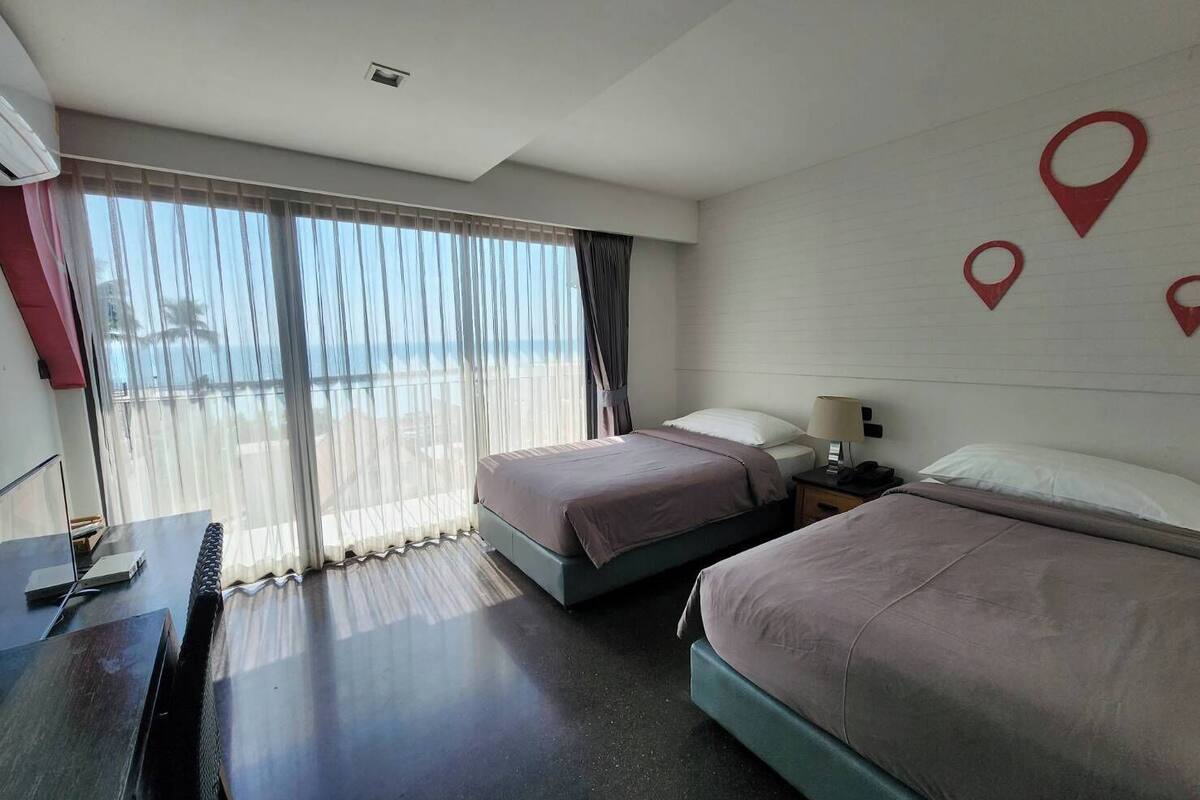 Habitación de hotel con dos camas, un escritorio y vista al mar.