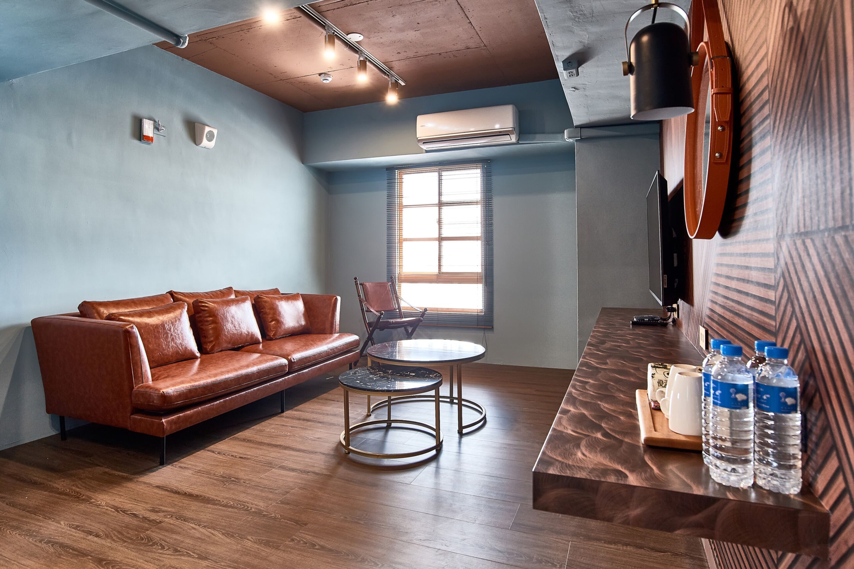 Una habitación moderna con un sofá de cuero, una mesa redonda y una encimera de madera con botellas de agua.