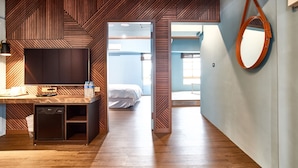 Una habitación de hotel moderna con piso de madera, un escritorio con silla, un mueble pequeño, una cama y un espejo grande en la pared.