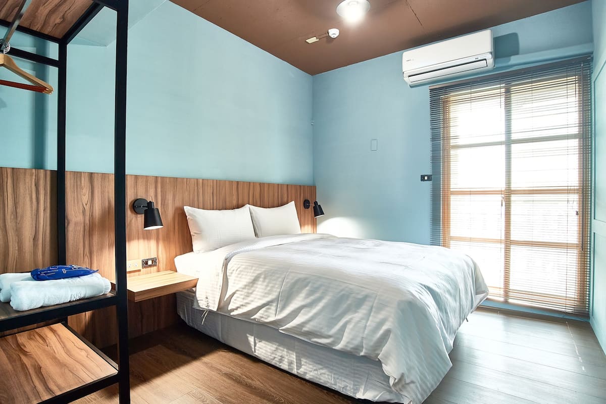 Ein Schlafzimmer mit Bett, Holz-Kopfteil, Nachttisch und einer Hängegarderobe mit Handtüchern.