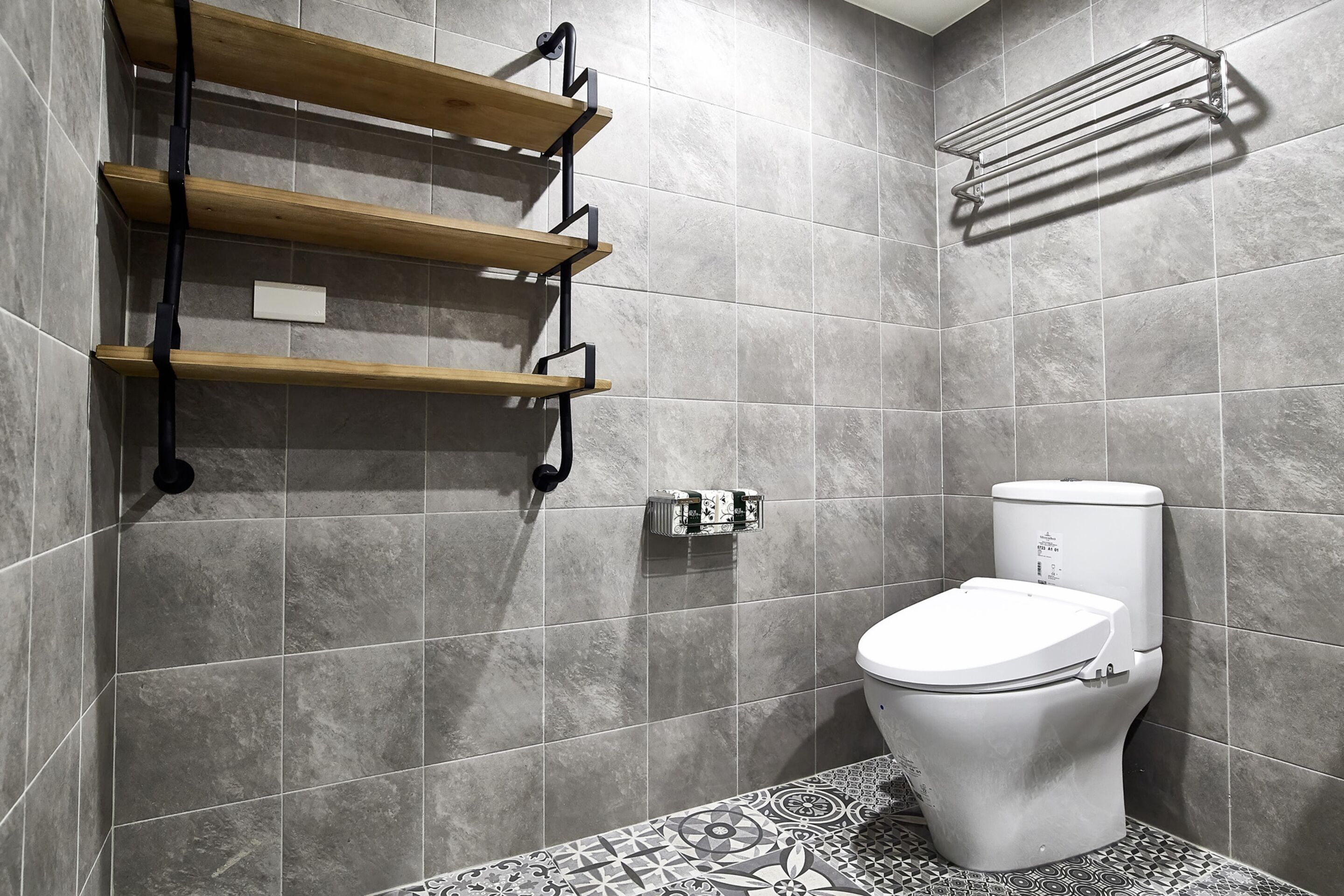 Un baño moderno con baldosas grises, un inodoro blanco y estantes de madera.