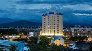 Un hotel de varios pisos con una torre central destacada, rodeado de otros edificios y un paisaje montañoso.