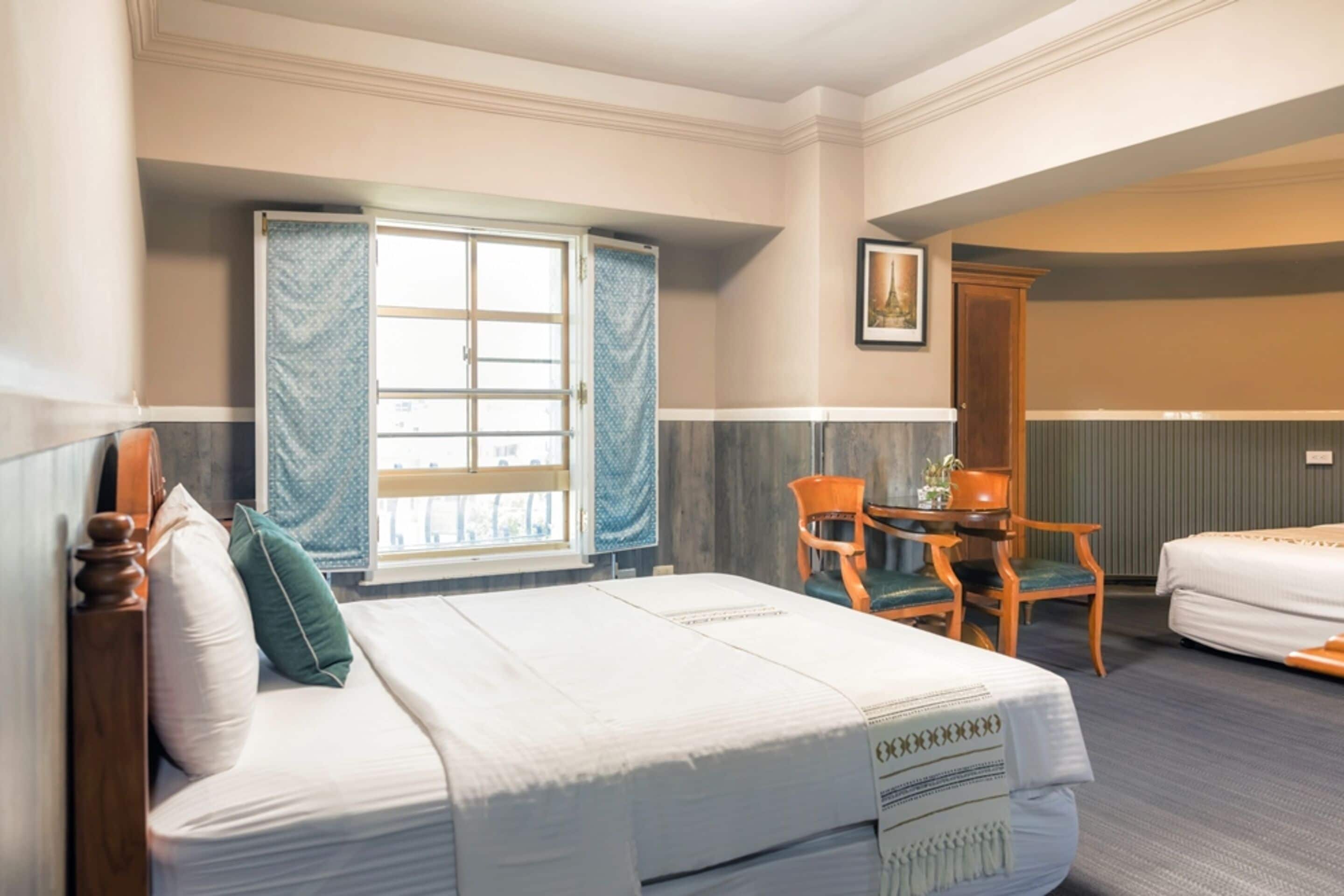 Ein Hotelzimmer mit Bett, Sessel, Tisch und einem Vorhangfenster.