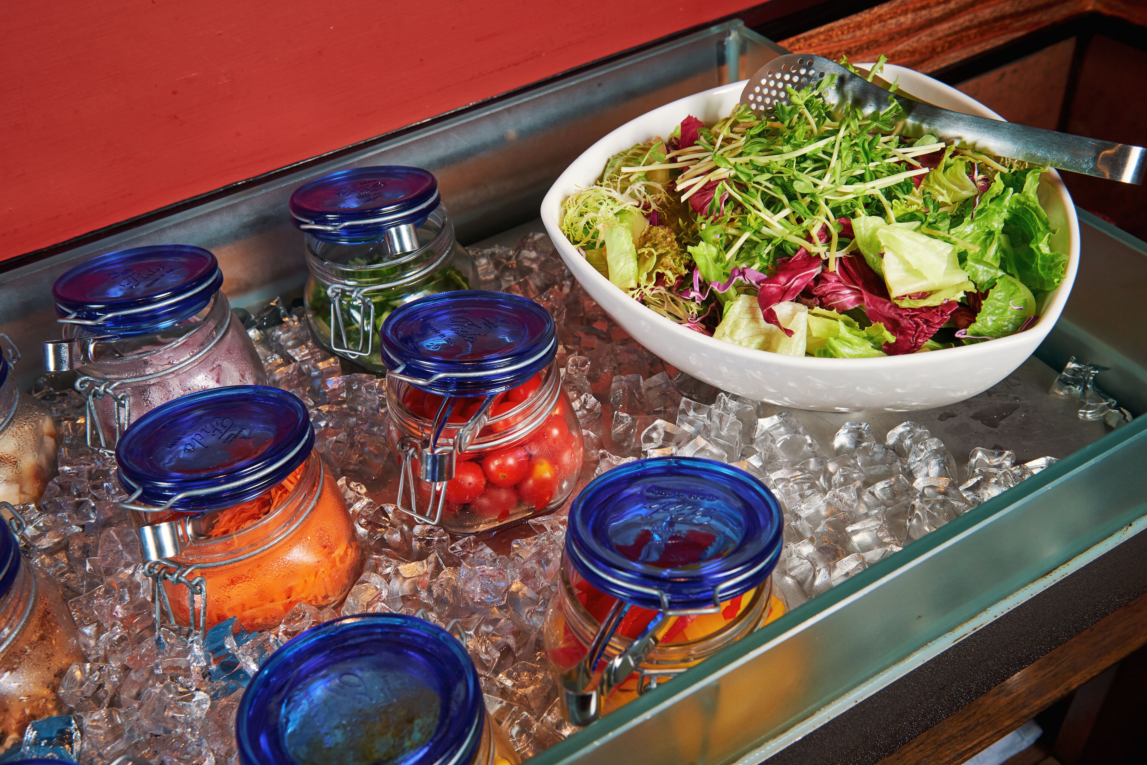 Un bufé con un bol de ensalada y diversos alimentos sobre hielo.