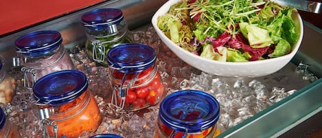Un bufé con un bol de ensalada y diversos alimentos sobre hielo.