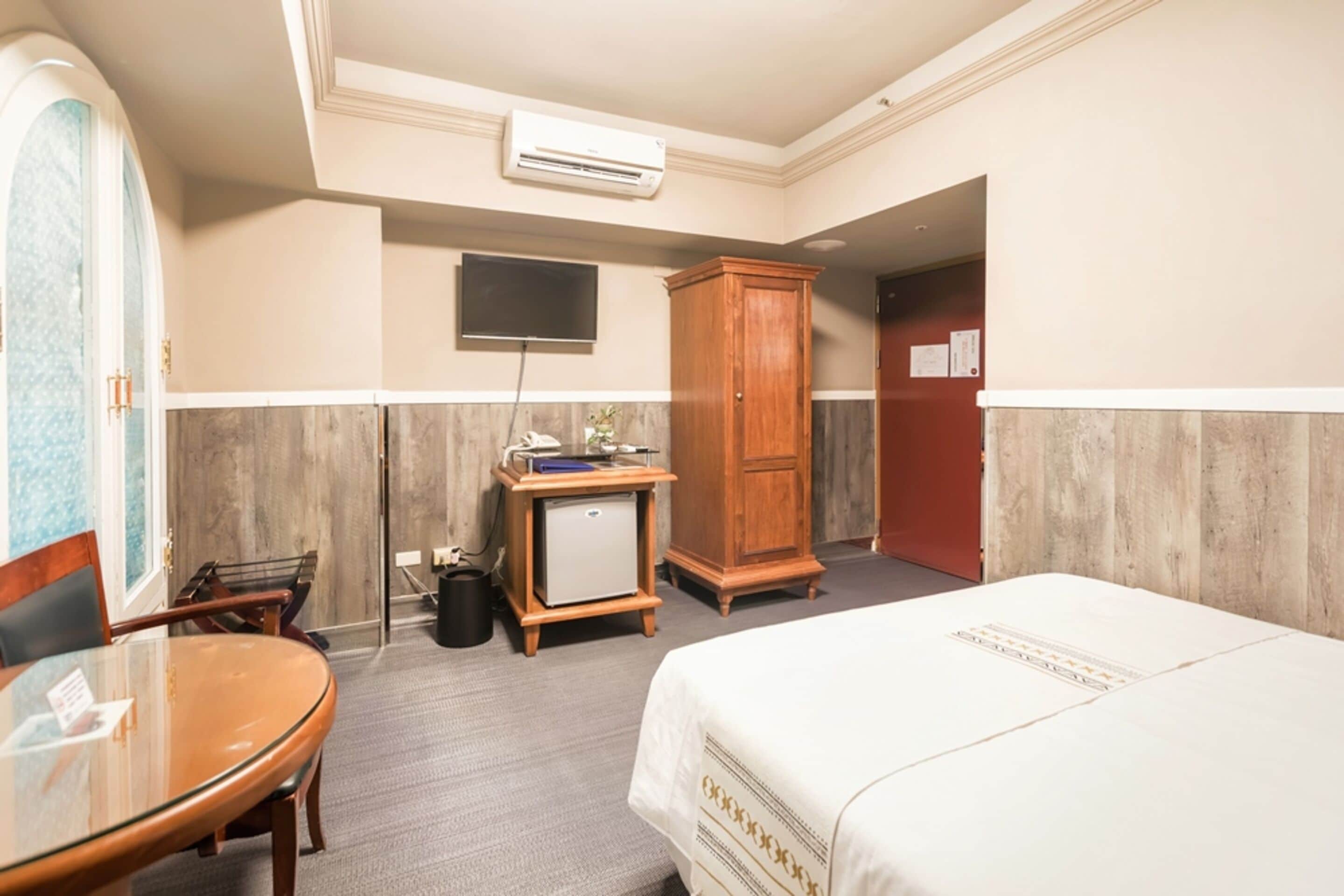 A hotel room with a bed, a desk, a chair, a wardrobe, and a television.