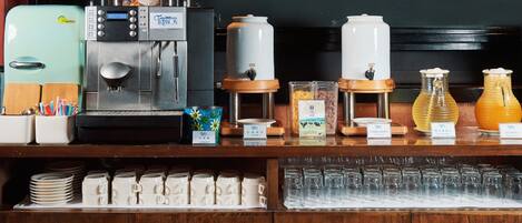 A coffee station with a coffee maker, milk frother, and various coffee dispensers.