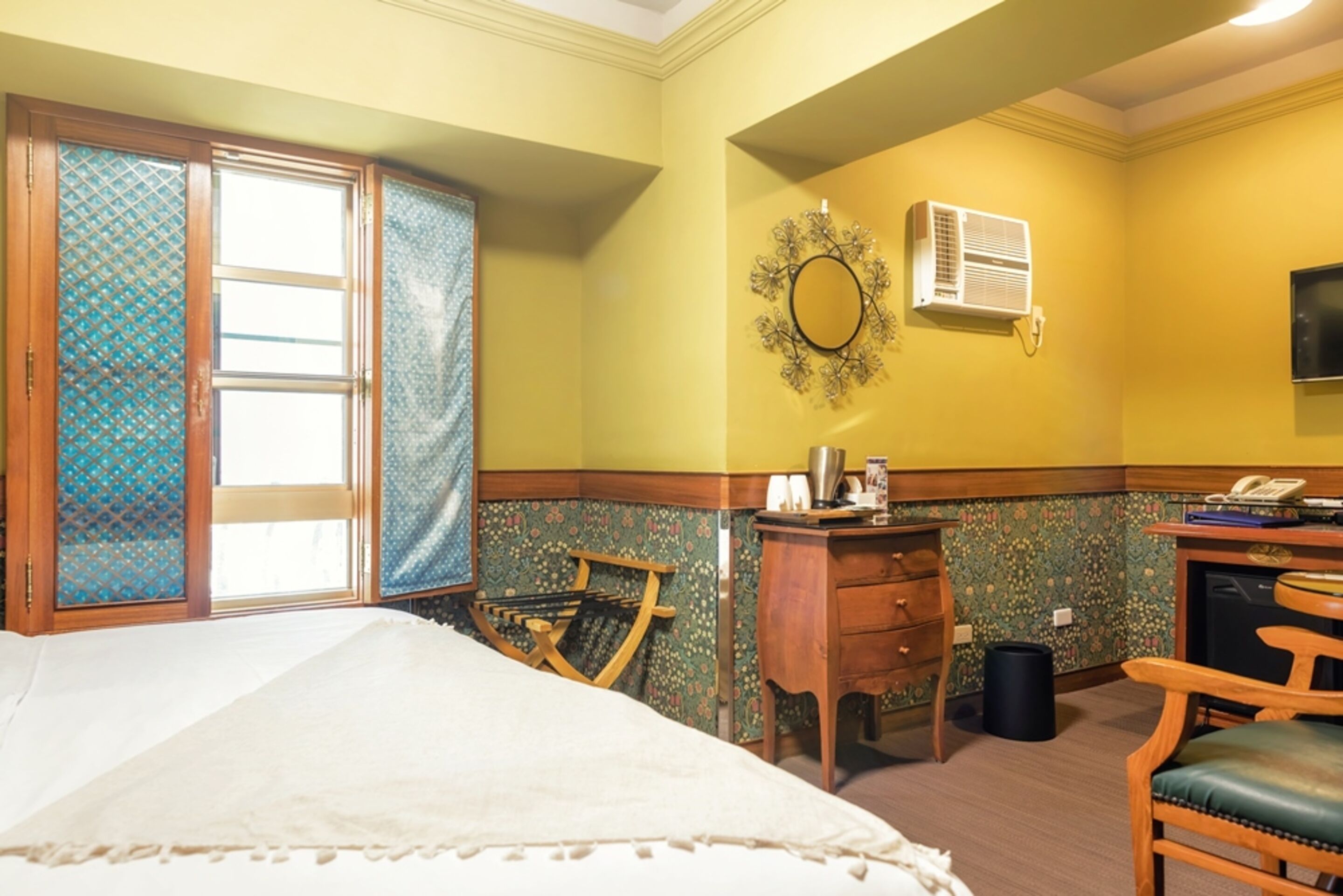 Une chambre d’hôtel équipée d’un lit, d’un bureau avec un téléphone, d’une chaise et d’un climatiseur fixé au mur.