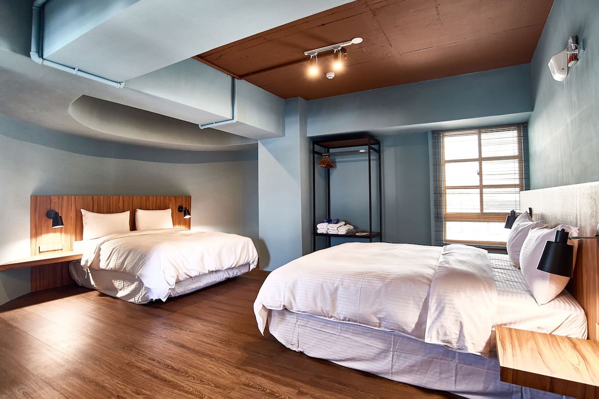 Ein modernes Schlafzimmer mit zwei Betten, Holzboden und einem großen Fenster.