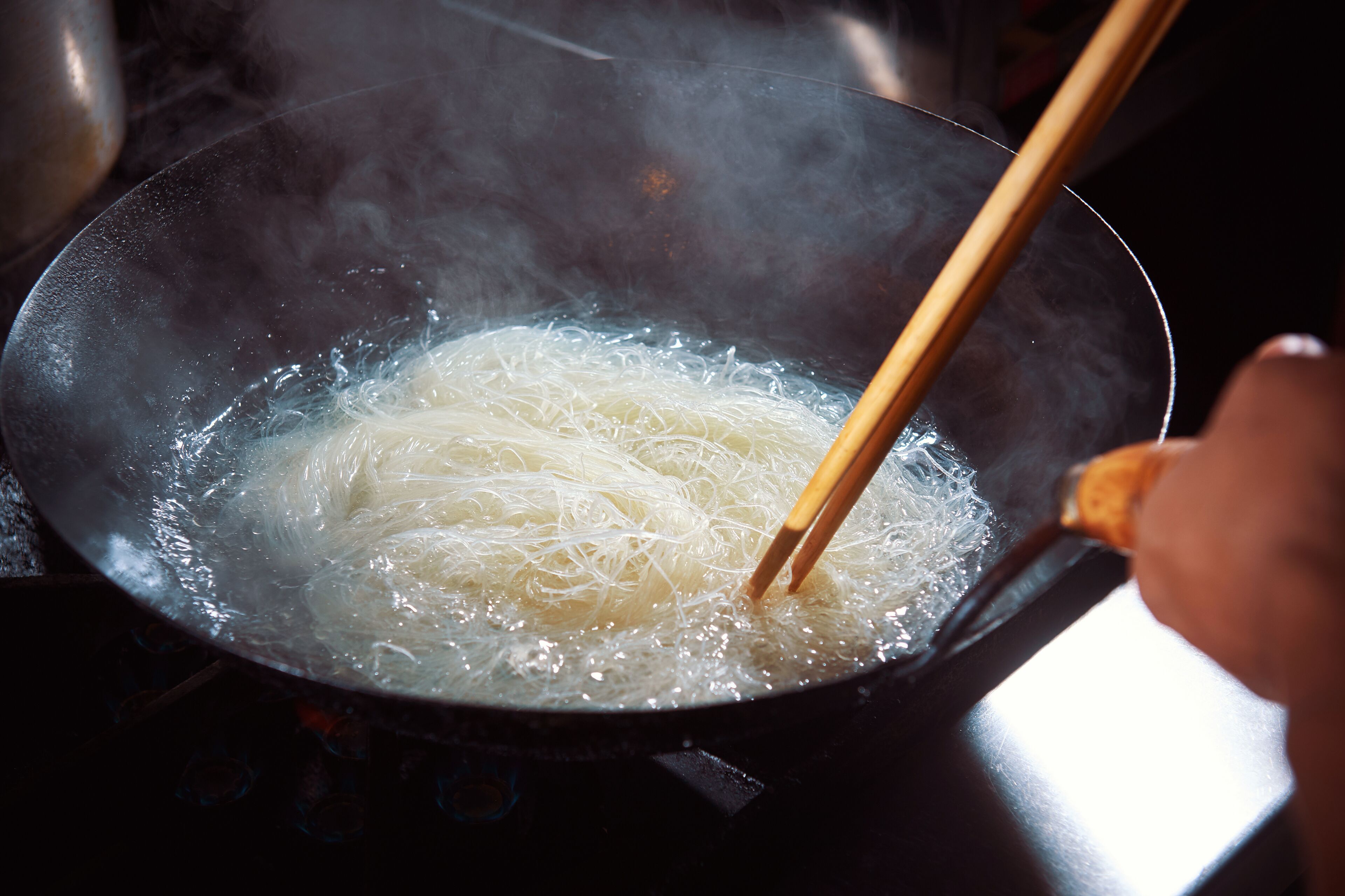 Noodles being stirred in a pan with chopsticks.
