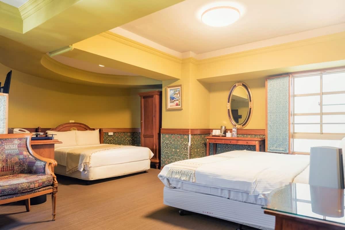 Ein Hotelzimmer mit zwei Betten, einem Holzstuhl, einem Nachttisch, einem Spiegel und einem Fenster.