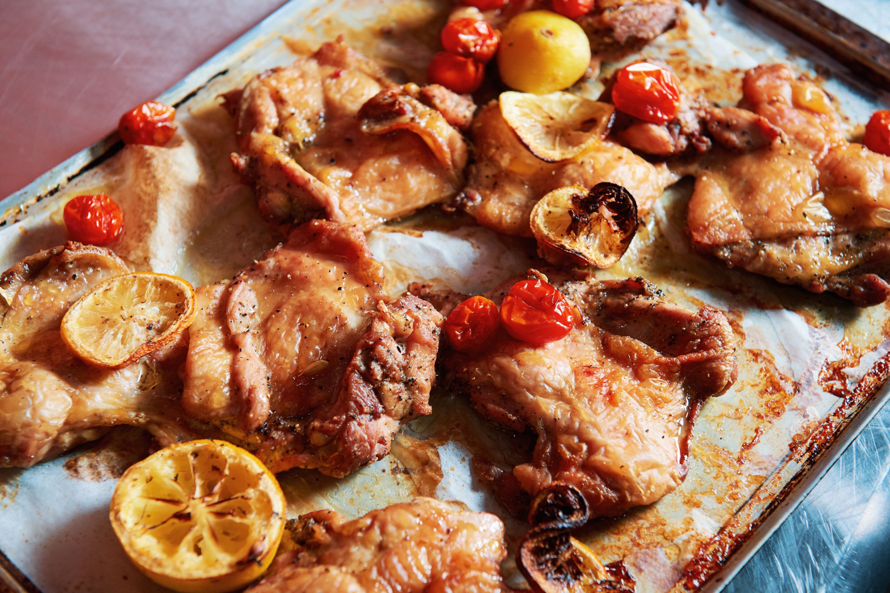 Un vassoio con pollo arrosto, fettine di limone e pomodorini.