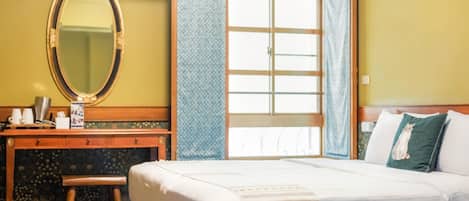 Habitación de hotel con cama, escritorio con espejo, taburete pequeño y ventana con cortinas.