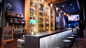Una zona de bar con una barra larga, taburetes y estantes llenos de botellas.