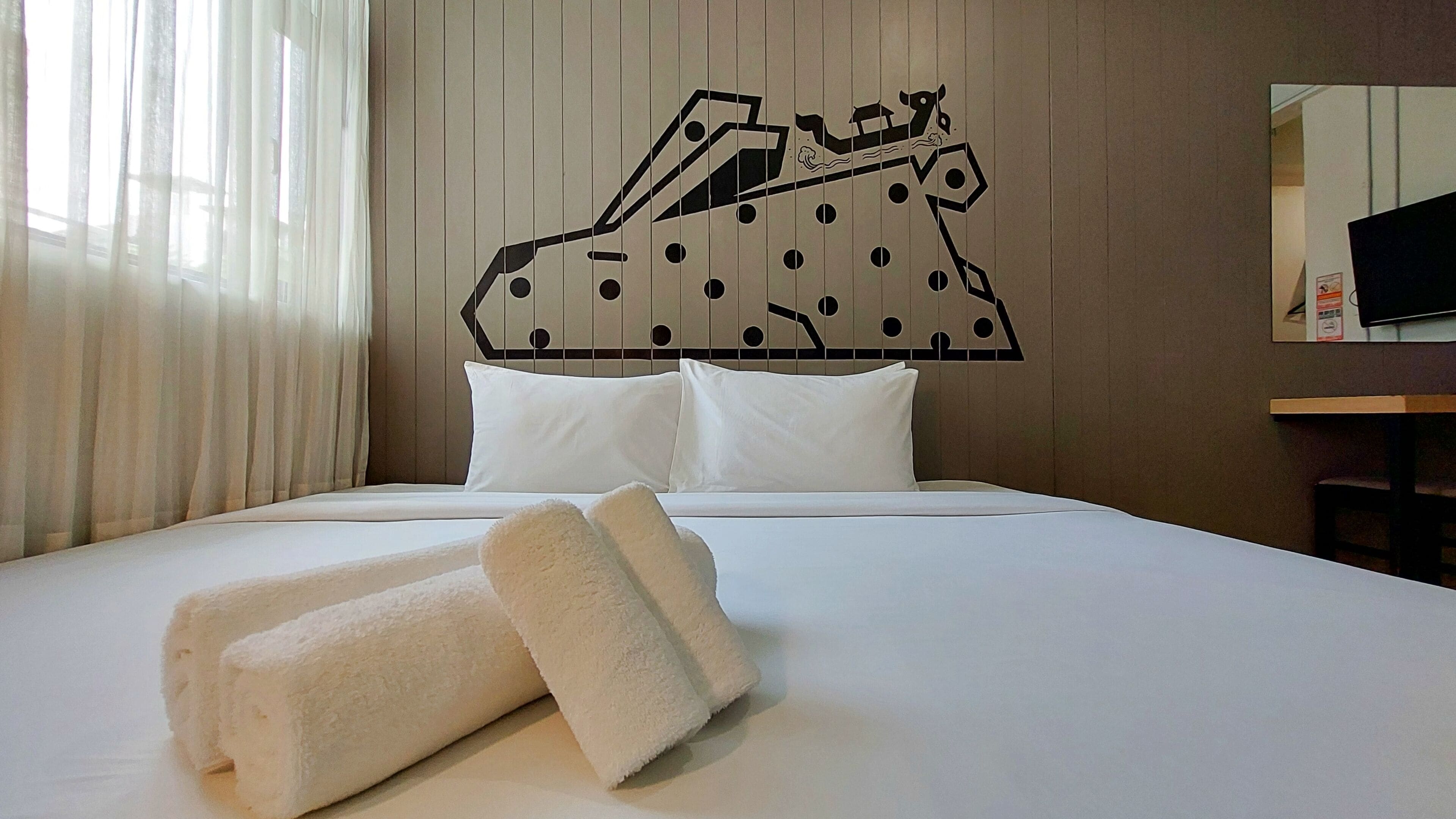 Una habitación de hotel con cama, almohadas blancas, una toalla y un adorno en la pared.