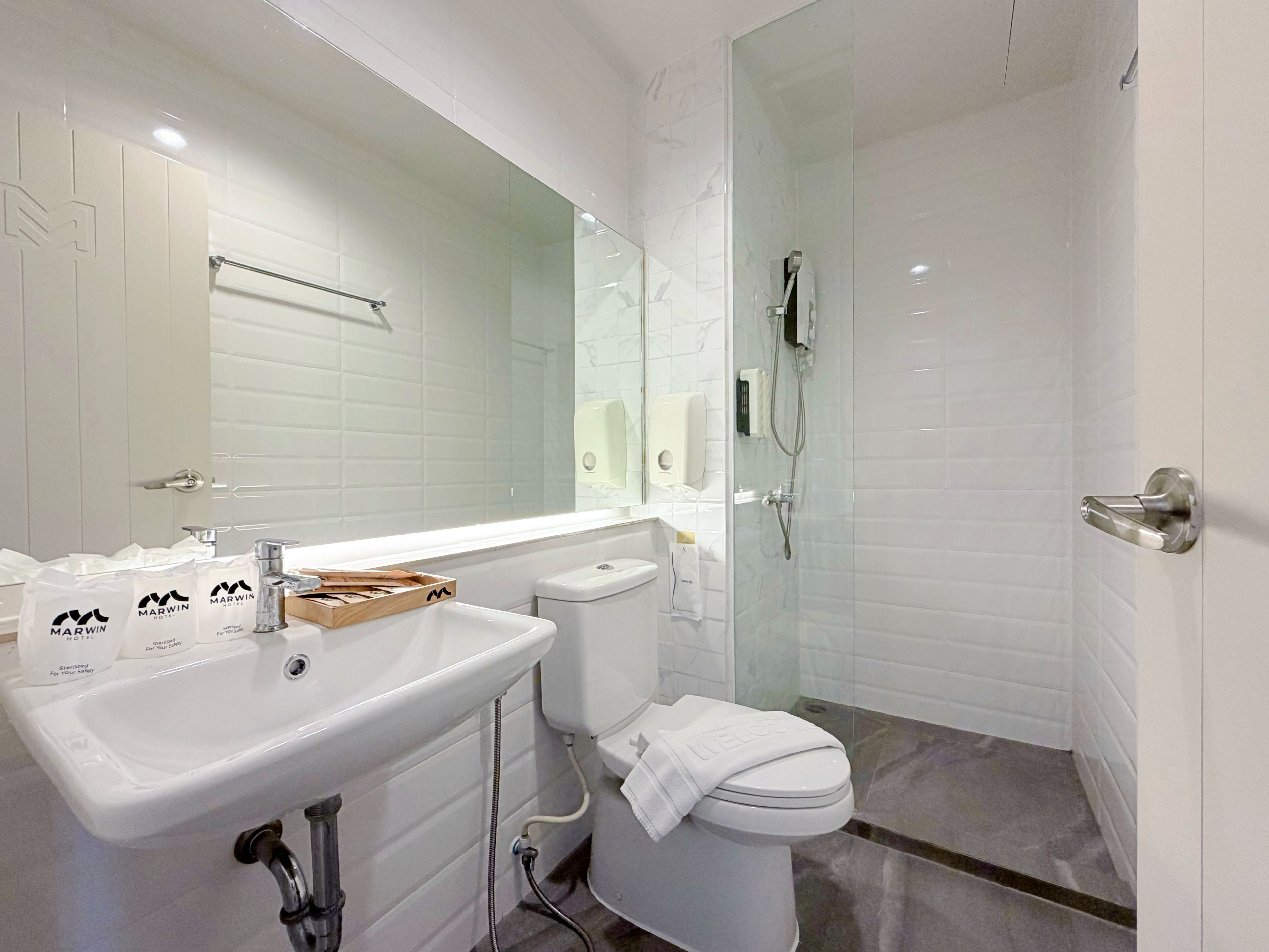 Un baño moderno con lavamanos blanco, espejo y ducha con mampara de vidrio.