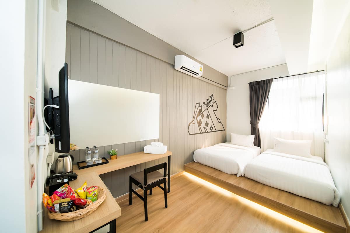 Ein Hotelzimmer mit Holztisch, zwei Betten, Fernseher, Wandklimaanlage und einem Vorhangfenster.