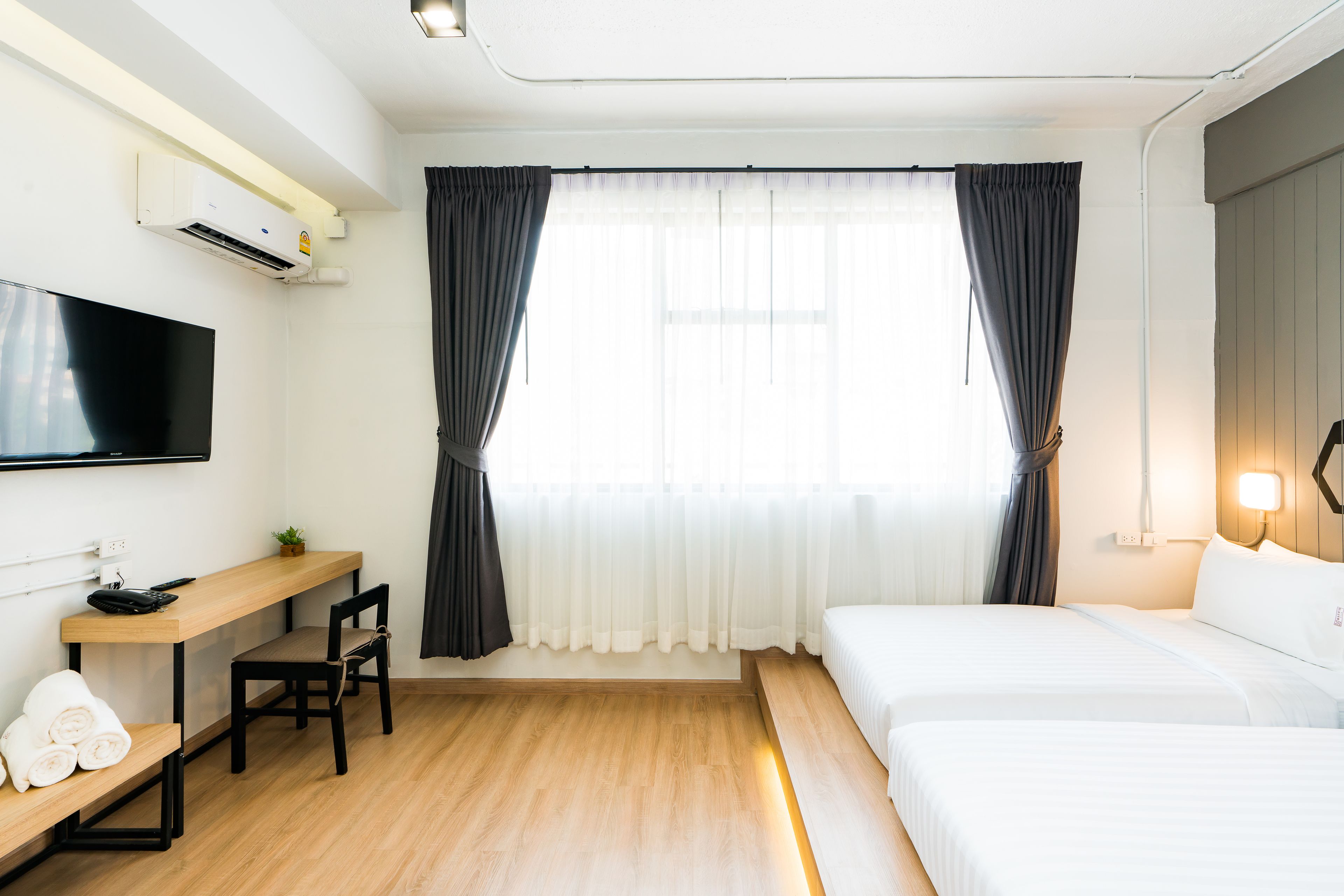 A hotel room with a bed, a desk with a chair, a TV, and a window with curtains.