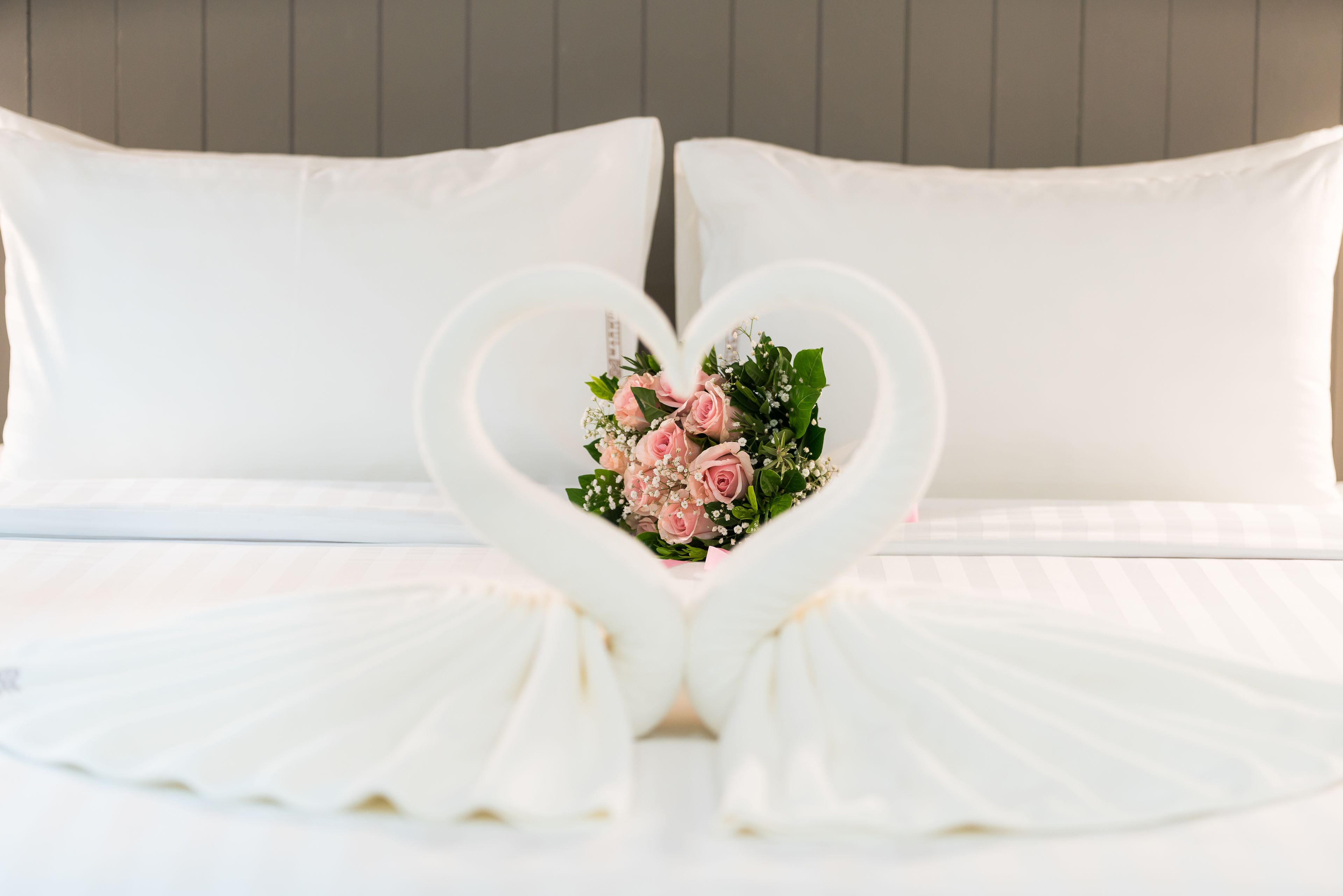A bed with white linens and pillows, a heart-shaped floral arrangement in the center, and a heart-shaped bed runner.