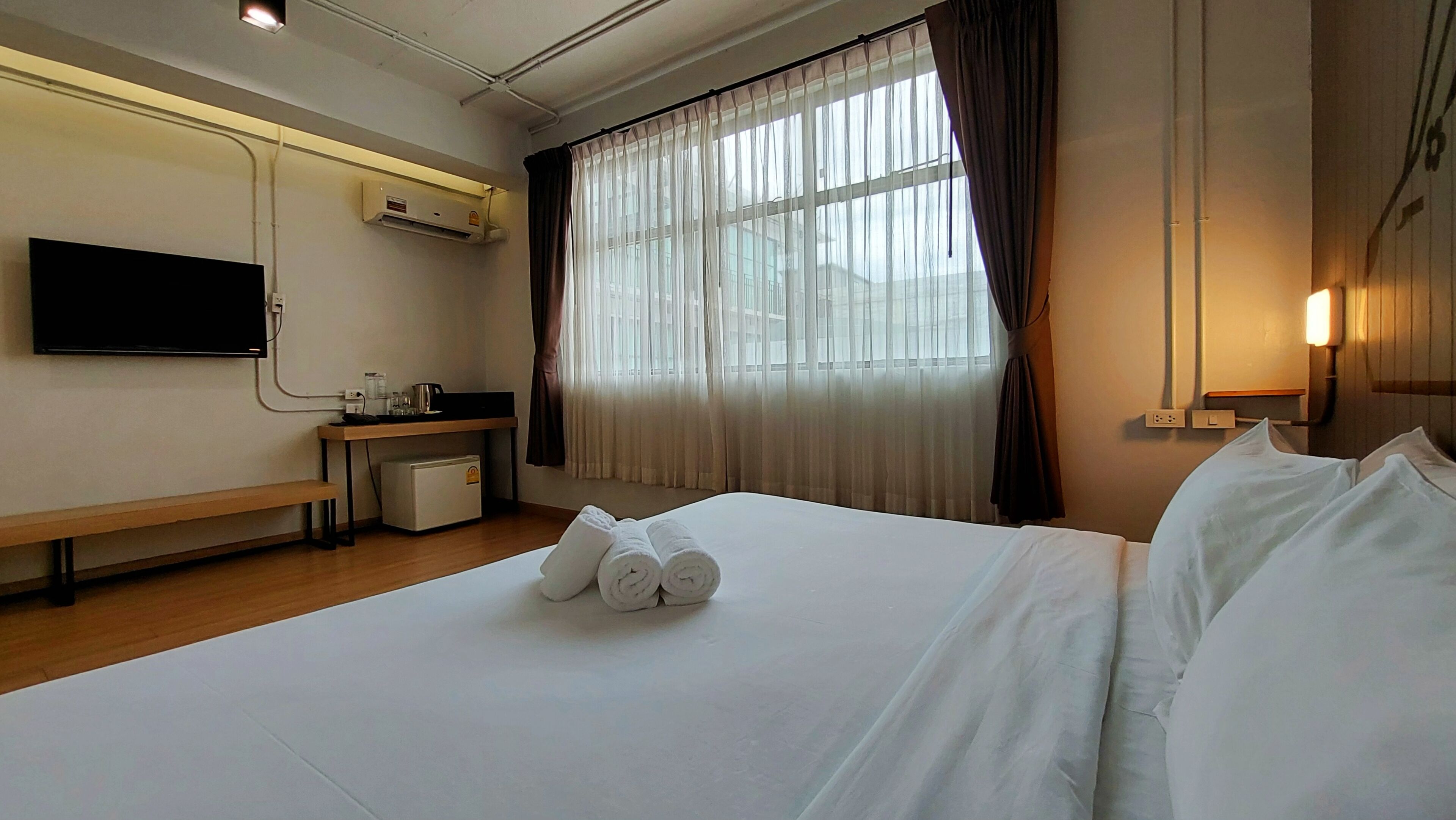 A hotel room with a bed, a desk, a television, an air conditioning unit, and a window with curtains.