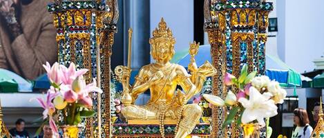 A golden statue of a deity surrounded by colorful mosaic decorations and flowers.