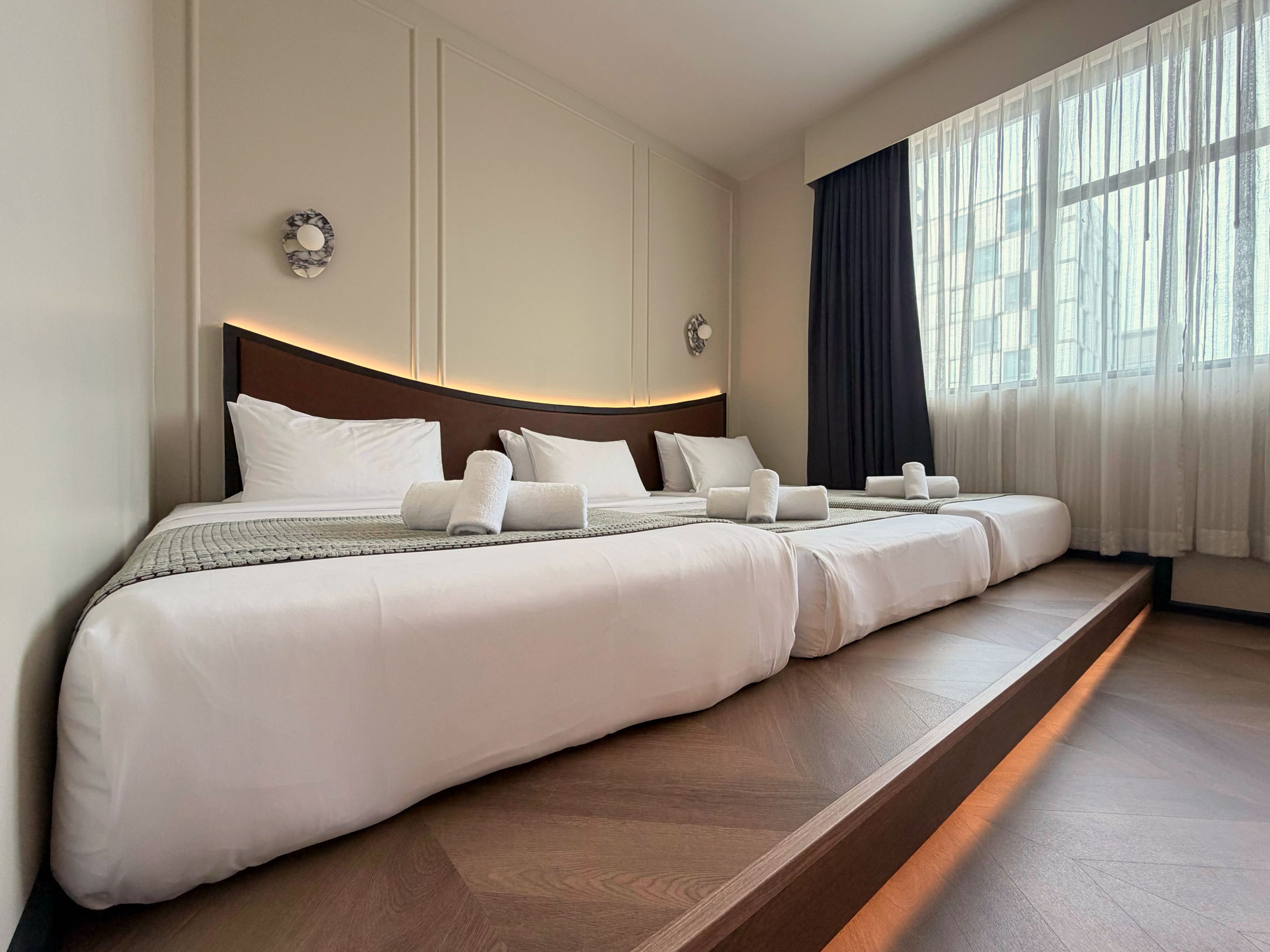 Una cama grande con cabecera de madera, ropa de cama blanca y una mesita de noche con una lámpara.