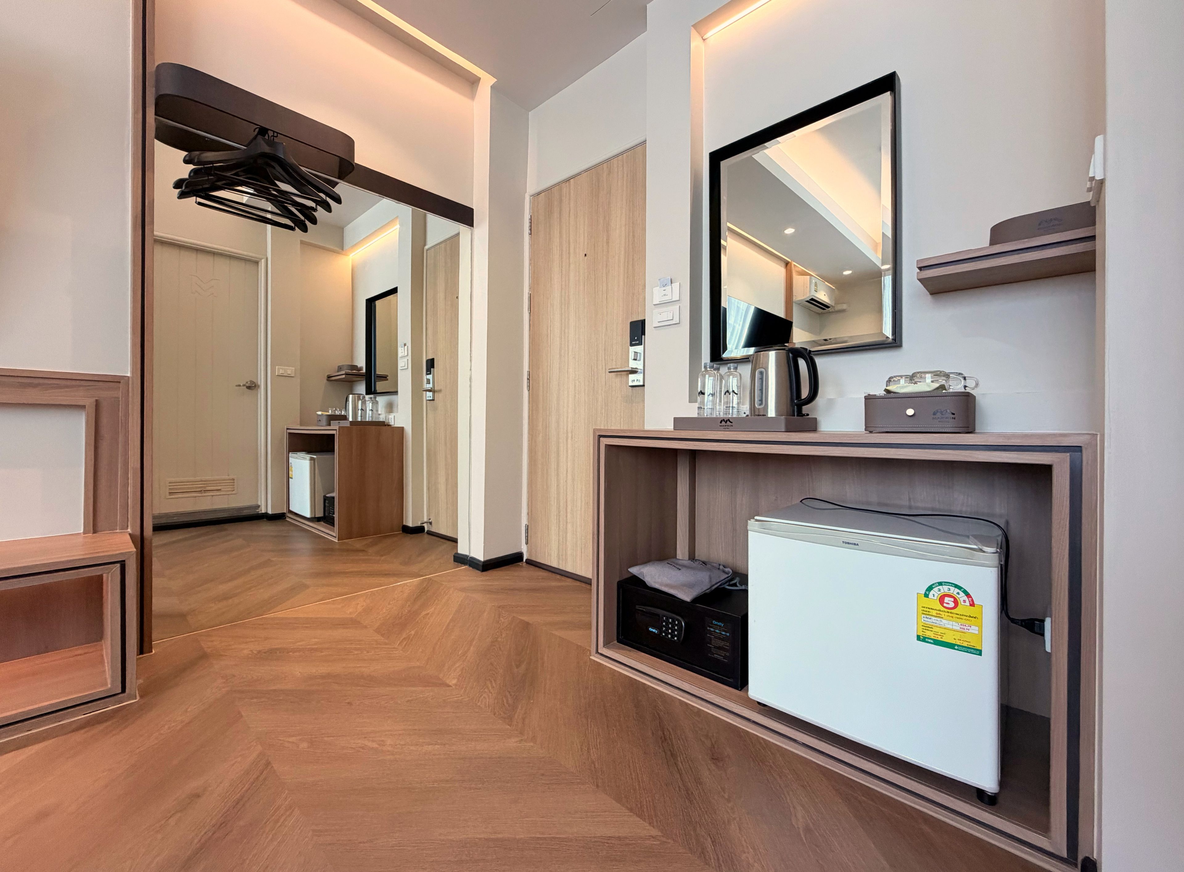 Habitació d'hotel amb terra de fusta, barra minibar, nevera, mirall i televisió.