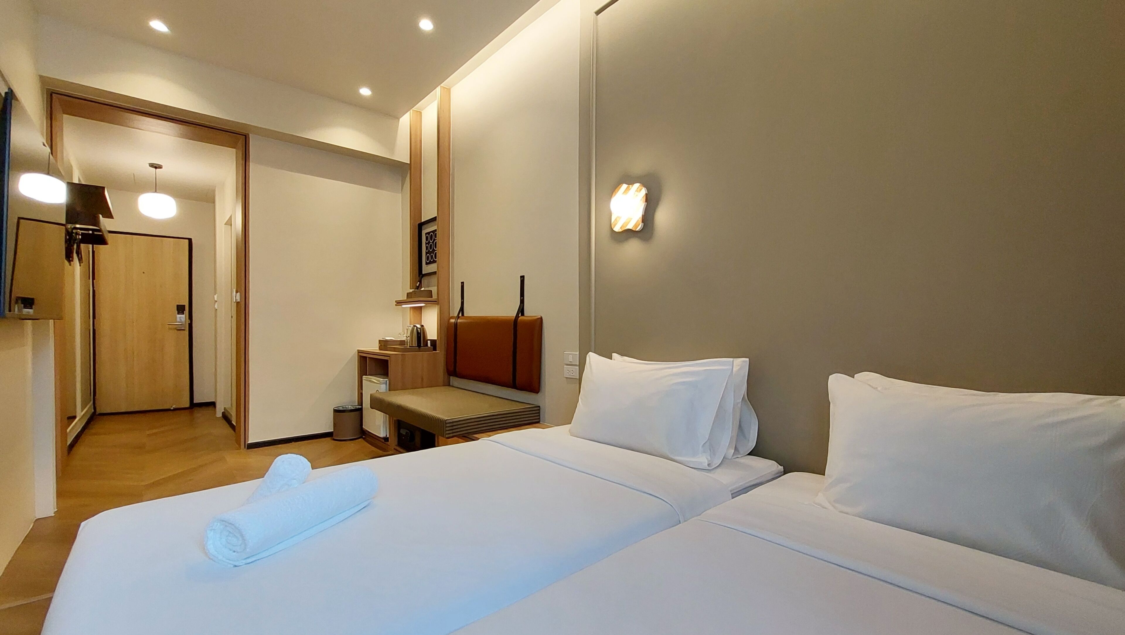 Habitación de hotel con dos camas, un escritorio, una silla, una mesita, un cubo de basura y una puerta.
