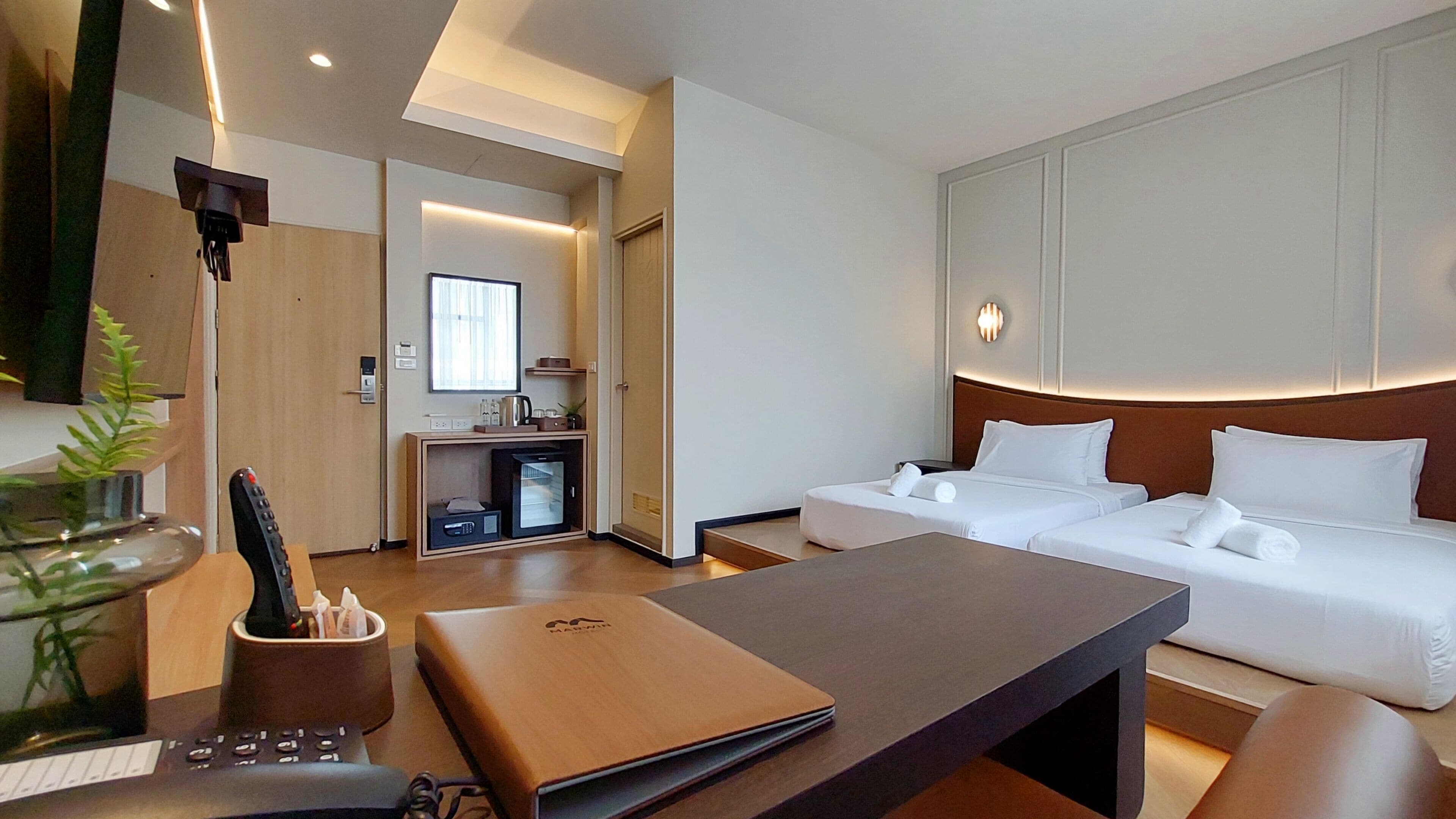 Quarto de hotel com uma cama, uma escrivaninha, uma máquina de café e uma pequena cozinha equipada.