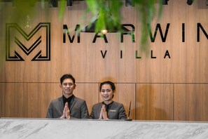 A reception desk with two staff members standing behind it. The wall behind the desk has the text "MARWIN VILLA" and a logo. - Marwin Villa (Bangkok)