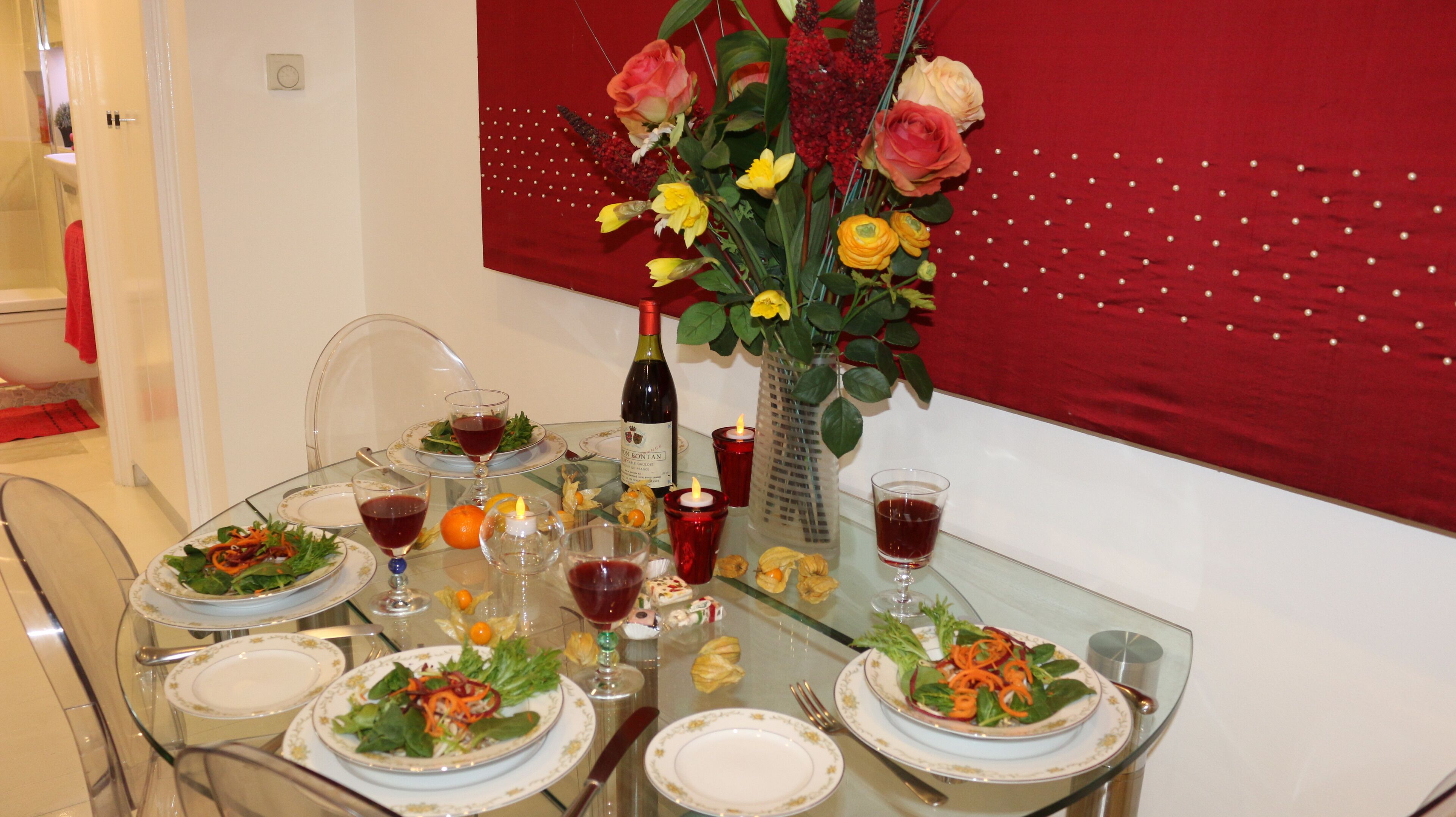 Taula de dinar posta amb plats, gots i una ampolla de vi, envoltada de flors decoratives i espelmes.