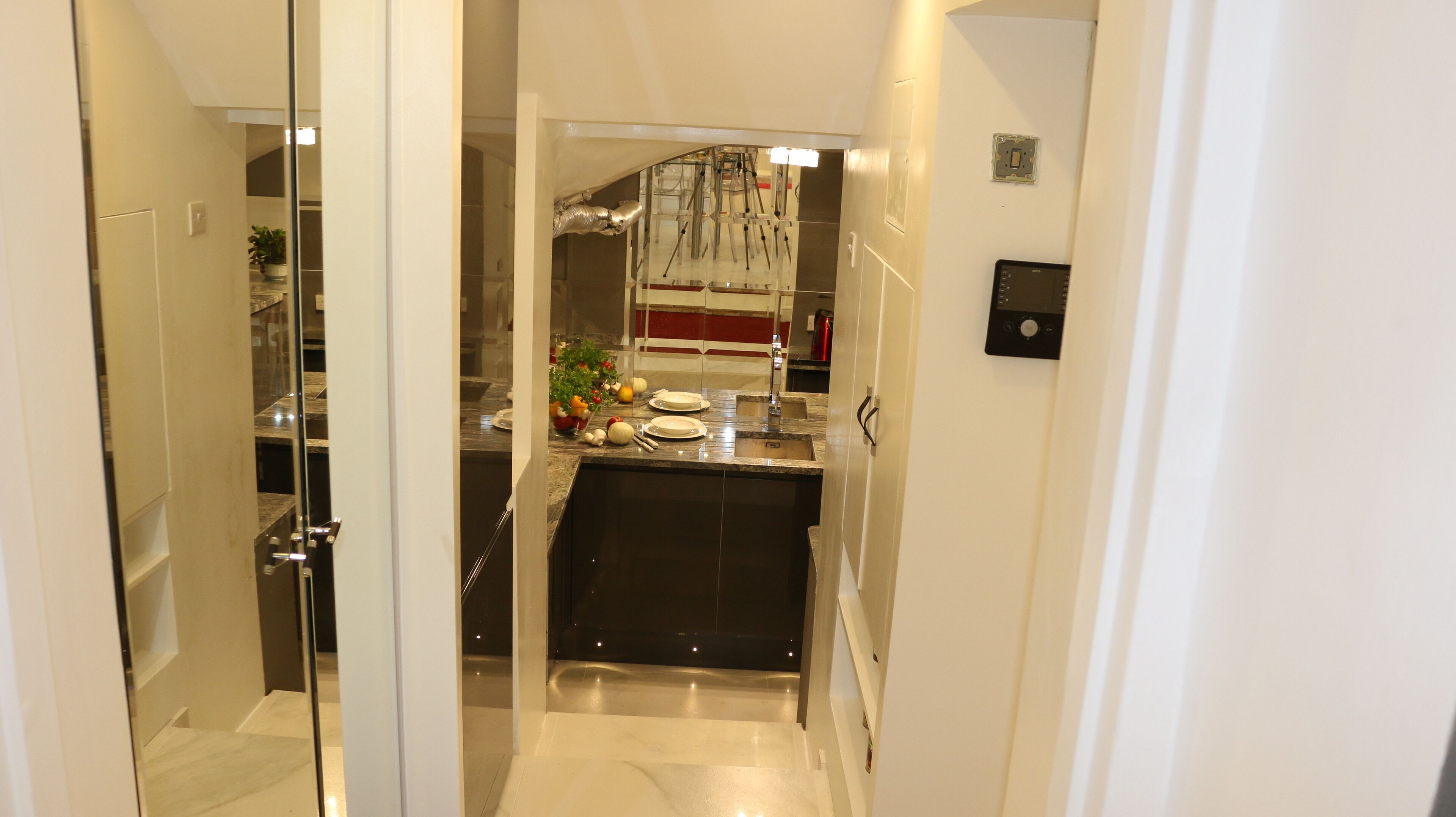 A narrow hallway leading to a kitchen with a marble countertop, a sink, and a stainless steel range hood.